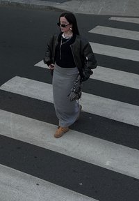Μαύρο μπουφάν, μαύρη μπλούζα, γκρι μάξι φούστα, καφέ μπότες. Τα αξεσουάρ περιλαμβάνουν κρεμαστά επιχρυσωμένα κολιέ από πέρλες και μικρή τσάντα χειρός. Περπατάει στη διάβαση.