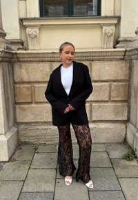 Blazer de gran tamaño negro sobre una camisa blanca ajustada, combinado con pantalones de encaje negro transparente de campana. Tacones abiertos blancos completan el look.