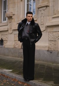 Czarna skórzana kurtka z futrzanym kołnierzem na szarym swetrze, w zestawie z czarnymi spodniami z wysokim stanem i błyszczącymi czarnymi butami.