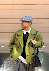 Groene wollen peacoat met grote knopen, gedragen over een zwarte trui en witte blouse; grijze platte pet en zwarte leren schoudertas.