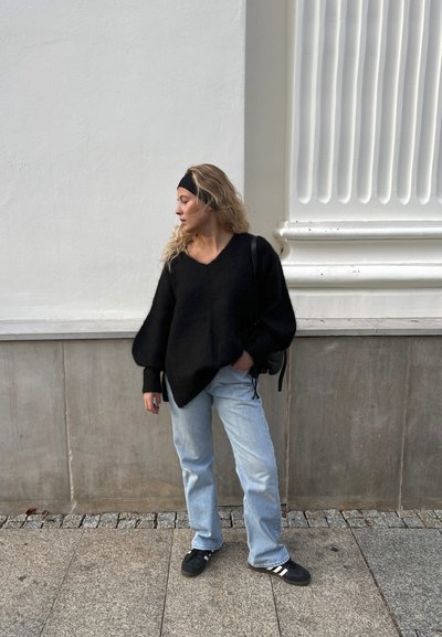 Suéter negro, esponjoso y de gran tamaño con escote en V y mangas abullonadas. Combinado con jeans rectos de color azul claro y zapatillas negras.