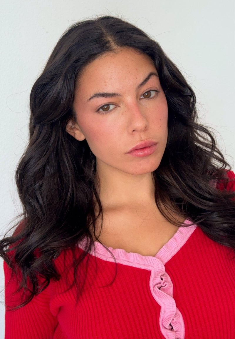 Cardigan rouge côtelé avec bordure à volants roses et boutons, doté d'un col en V et de manches longues, porté par une personne aux longs cheveux foncés.