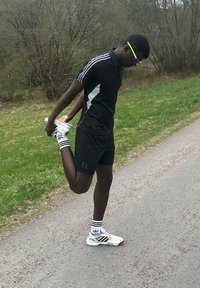 Fekete sportos rövidnadrág és egy hozzáillő póló fehér csíkokkal, fehér sportcipő és csíkos zoknik. A személy nyújtja az egyik lábát.