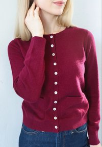 Vuneni kardigan bordo boje s okruglim izrezom, prednjim zatvaračem na kopčanje i dva džepa. Ima bijele gumbe i rebraste manžete.