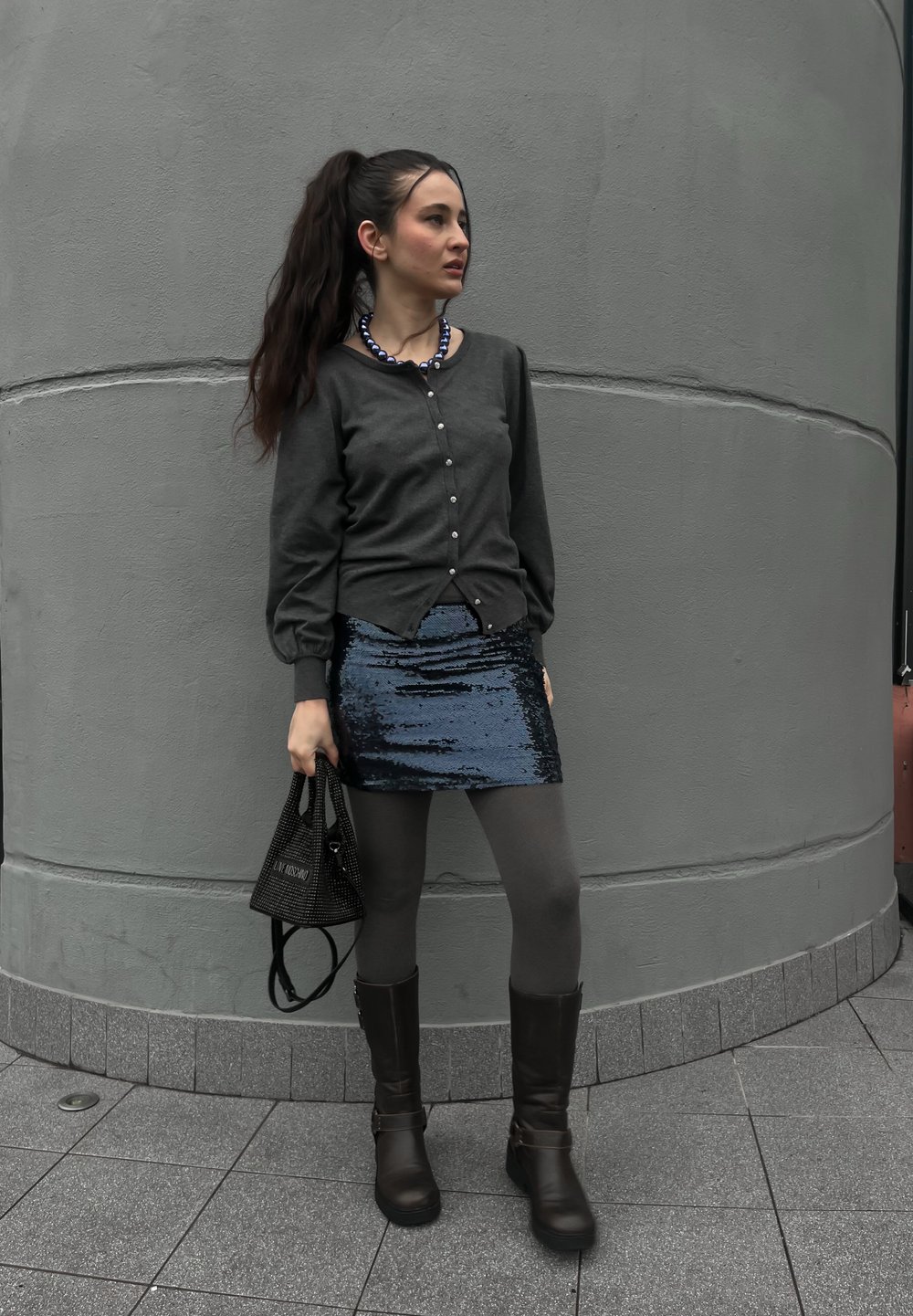 Γκρι πουκάμισο, μπλε μίνι φούστα με παγιέτες, γκρι καλσόν, καφέ μπότες μέχρι το γόνατο και μαύρη τσάντα από τούλι. Απλά κοσμήματα ολοκληρώνουν την εμφάνιση.