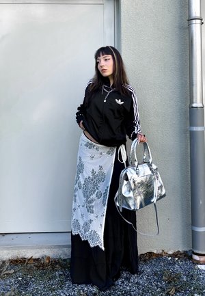 Veste de sport noire avec des rayures blanches, jupe blanche à fleurs et sac à main argenté brillant. Design simple, textures superposées et couleurs contrastées.