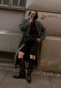 Pilkas per didelis vilnonis paltas, juodas viršus ir šortai iki kelių; juodi odiniai aulinukai su smailiais galiukais, juoda rankinė per petį ir kailio ausinės.