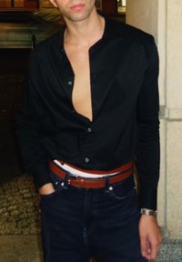 Camisa negra con cuello abierto, detalle de botones y mangas largas. Combinada con vaqueros oscuros y cinturón marrón. Ambiente urbano informal.