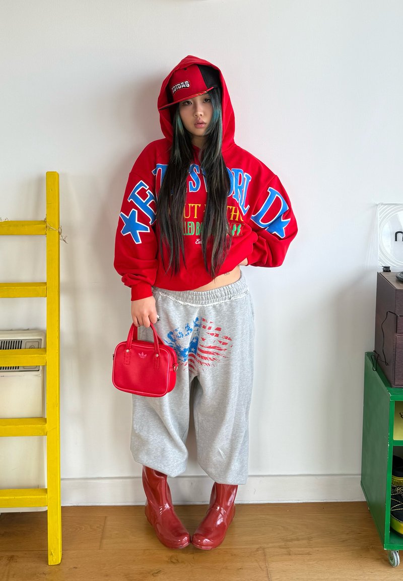 Red oversized hoody with blue and green text, grey joggers with a red and blue pattern, red handbag, and shiny red boots.