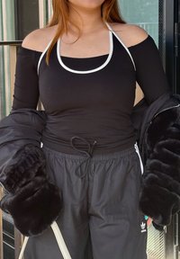 Sort langærmet off-shoulder top med hvid kant, parret med sorte sweatpants med snøre og falsk pelsdetaljer på ærmerne.