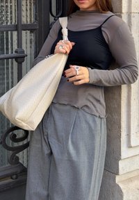 Schichtoutfit mit einem grauen Langarmoberteil über einem schwarzen Cami, kombiniert mit lockeren grauen Hosen. Trägt eine große beige gesteppte Handtasche.