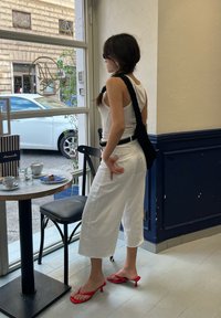 Λευκά κοντά παντελόνια, εφαρμοστό μαύρο ζωνάκι, λευκό μπλουζάκι αμάνικο, μαύρη τσάντα ώμου, κόκκινες γόβες. Μάρμαρο τραπέζι με φλιτζάνια καφέ και ένα γλυκό στο προσκήνιο.