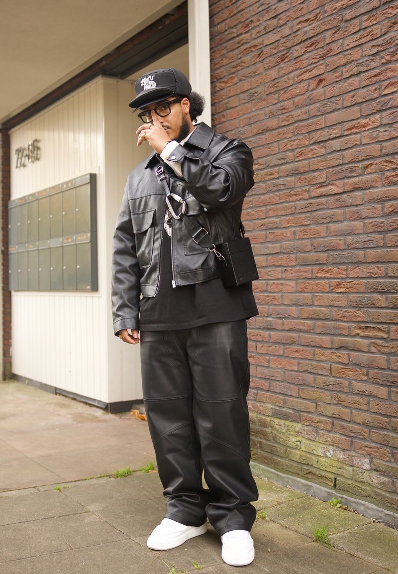 Veste en cuir noire avec poches, pantalon en cuir assorti et baskets blanches. Accessoires inclus un sac noir et une casquette noire.