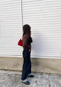 Asmuo vilki rudą megztinį ir platėjančius tamsiai mėlynus džinsus su apvadu, derindamas su juodais batais ir raudona petneša.