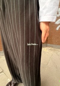 Sorte stribede bukser med hvide striber, der har en broderet tekst "iets Frans..." på benet. Blødt stof og afslappet pasform.