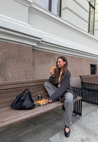 Svart skinnveske, grå strikket cardigan, grå bukser; trebenk; gyldne croissanter på et brett; mørk kaffekopp med lokk; steinbelagt fortau.