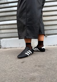 Scarpe da calcio nere con strisce bianche, realizzate in pelle liscia con un design a profilo basso. Indossate con calzini neri alla caviglia.