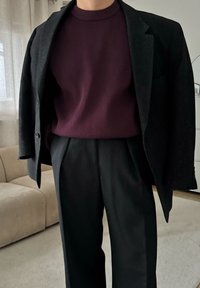 Blazer noir sur un pull côtelé violet foncé, associé à un pantalon noir coupé sur mesure. Textures lisses dans un design ajusté.