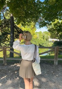 Λευκή, μακρυμάνικη μπλούζα με κορδόνι, συνδυασμένη με πτυχωτή, καφέ καρό φούστα. Μαλλιά πιασμένα σε σινιόν με κλιπ σε σχήμα πεταλούδας. Λευκή τσάντα ώμου.