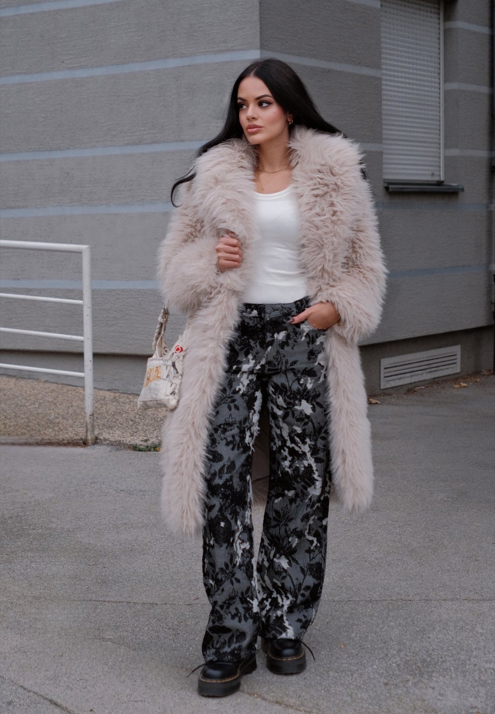 Hosszú, puha bézs műszőrme kabát, fehér felső, fekete virágmintás, bőszárú nadrág és vastag fekete platform cipők. Keresztpántos táska is tartozik hozzá.