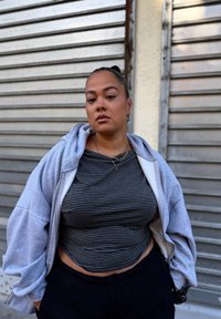 Sivi dukserica preko crno-bijelog prugastog topa, u kombinaciji s crnim hlačama. Subjekti nose slojevite ogrlice i stylish frizure.