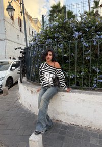 Czarno-biały, oversize'owy sweter w paski z odkrytymi ramionami, zestawiony z jasnoniebieskimi dzwonami i czarnymi sandałami na obcasie.