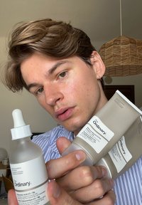 Tre prodotti per la cura della pelle di The Ordinary: una bottiglia in vetro con pipetta e un coperchio bianco, e due tubi beige etichettati con testo nero.