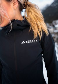 Črna jakna Terrex z teksturirano površino, visokim ovratnikom in polnim zadrgo. Ima bel logotip na prsih.
