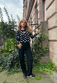 Sort og hvid prikket cropped sweater med nøglehul detalje, kombineret med sorte vide bukser og sorte sneakers. Grønne planter i baggrunden.