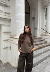 Rjav volna pulover z rebrastimi manšeti, v kombinaciji z ohlapnimi, temnimi usnjenimi hlačami. Majhna rjava torbica dopolnjuje obleko. Koraki in ozadje stolpa.