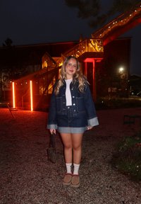 Jeansjacke mit hellblauen Manschetten, weißem T-Shirt, Jeansrock, beigen Hausschuhen, brauner Handtasche, im Freien mit beleuchteten Treppen.