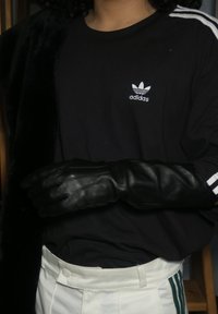 Czarna koszulka Adidas z białym logo, w połączeniu z czarnymi skórzanymi rękawicami. Białe spodnie mają zielone paski po bokach. Miękki czarny materiał zwisa.