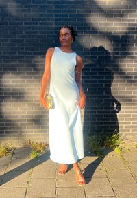 Svetlomodré, bezrukávové maxi šaty s hladkou štruktúrou. Nosička drží zlatú spojku. K outfitu sa hodia sandále v nude farbe s remienkami.