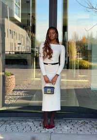 Lichtgrijze getailleerde jurk met lange mouwen en een zwarte riem, gecombineerd met een kleine zwarte handtas en bordeauxrode hakken. Gewatteerd oppervlak en slank ontwerp.