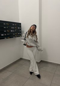 Lys grå genser og matchende joggebukser, myk tekstur, avslappet passform, brukt med en svart lue og briller, i en minimalistisk gang.