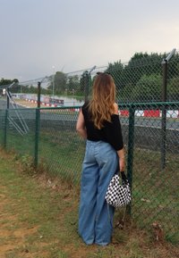 Φαρδιά, ανοιχτό γαλάζια τζιν παντελόνια συνδυασμένα με μαύρο τοπ και καρό τσάντα. Στη φοντογραφή περιλαμβάνονται ένας φράκτης και πράσινα φυτά.