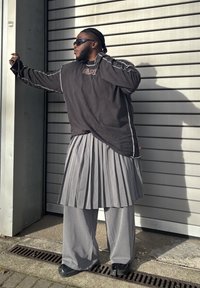 Nadmierne čierne tričko s dlhým rukávom s bielym prešívaním, v kombinácii so sivou skladanou sukňou a širokými nohavicami. Čierne slnečné okuliare a topánky.