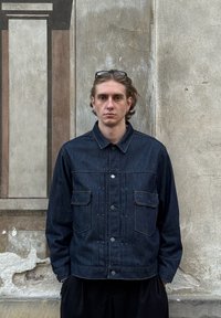 Mørkeblå denimjakke med knaplukning foran, to brystlommer og detaljerede syninger. Har en klassisk krave og afslappet pasform.