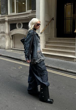 Jeansjacka och oversized byxor i mörkblått, grå topp och knähöga svarta stövlar med silverknappar; bärs med solglasögon och en svart väska.