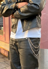 Veste en cuir noire avec zip, t-shirt blanc en dessous et pantalon noir orné de chaînes étoilées métalliques. Surface texturée avec un léger éclat.