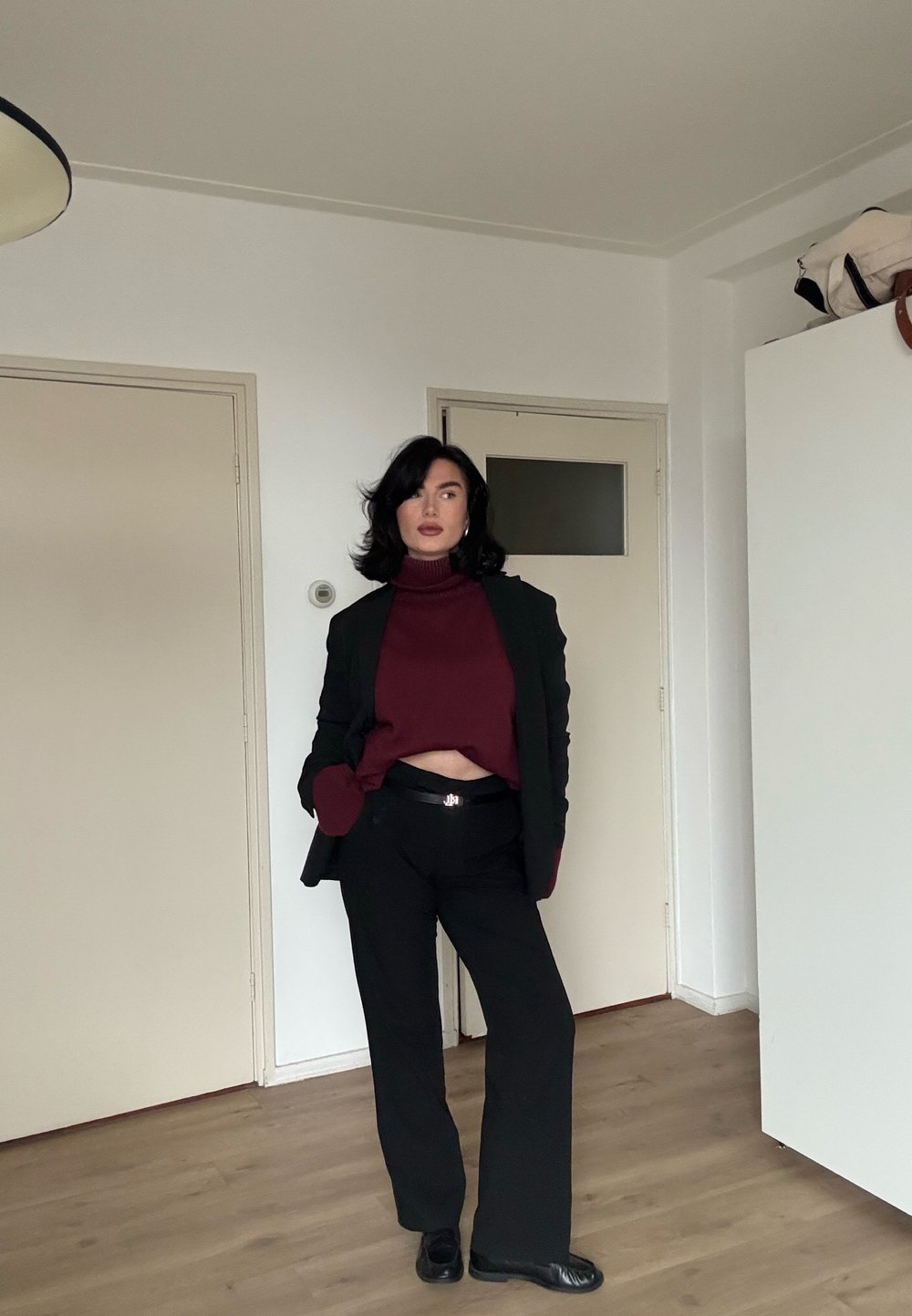 Pantalon noir associé à un col roulé court bordeaux et un blazer noir assorti. La tenue présente une finition lisse et un design sur mesure.