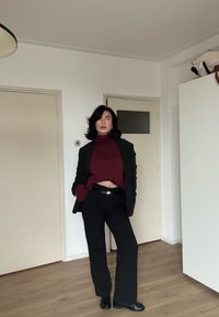 Pantalon noir associé à un col roulé court bordeaux et un blazer noir assorti. La tenue présente une finition lisse et un design sur mesure.