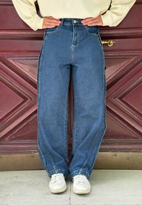 Højtaljede, lige ben blå jeans med falmet tekstur, kontrasterende syninger og sidelommer. Parret med hvide sneakers.