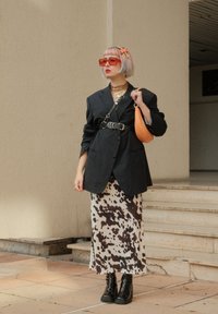 Sort oversized blazer, cowprint midi-nederdel, kraftige sorte støvler, orange håndtaske, røde solbriller, lagdelte guldhalskæder, pastelfarvet hår.