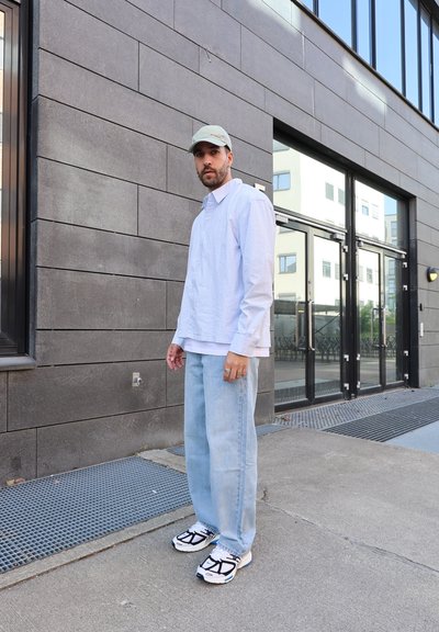 Camisa de botón a rayas celestes sobre una camiseta blanca, combinada con jeans celestes y zapatillas en blanco y negro. Una gorra gris acentúa el atuendo.