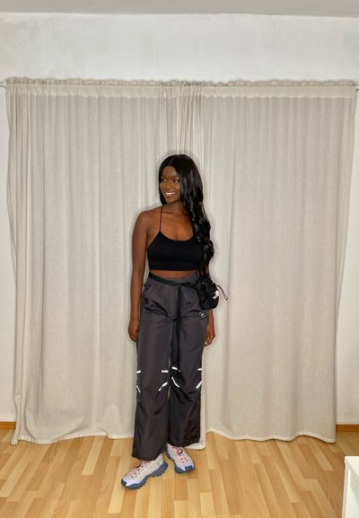 Top corto negro, pantalones de chándal negros de corte holgado con rayas reflectantes y zapatillas gruesas en gris y rojo. Textura suave y diseño casual.