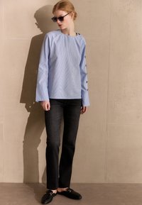 Hellblau gestreifte Bluse mit langen Ärmeln und Knopfdetails, kombiniert mit schwarzen geraden Jeans und schwarzen Mokassins. Glatter Stoff, lockere Passform.