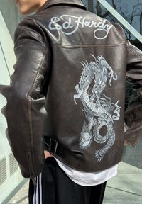 Hnedá kožená bunda s dizajnom strieborného draka na chrbte a logom "Ed Hardy" na ramene. Obsahuje zipsy a detaily opasku.