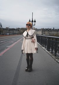 Hvit kjole med stor svart krage og snøring, kombinert med knelange svarte snørestøvler. Tilbehør inkluderer en liten veske og solbriller.