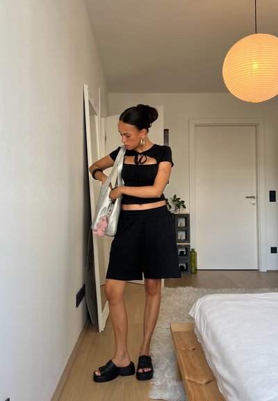 Top corto negro con diseño recortado y mangas cortas, acompañado de pantalones cortos negros holgados. Bolsa plateada con un charms de conejito rosa, sandalias de plataforma negras.